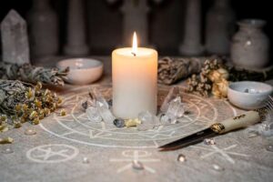 Brennende weiße Kerze auf dunklem Hintergrund, umgeben von Kristallen und Kräutern für spirituelle Rituale und Schutzmagie.