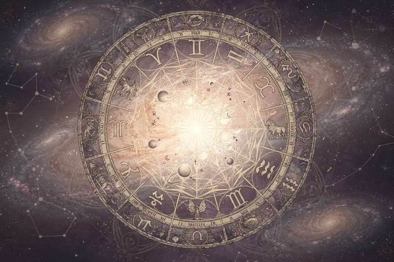 Frau sitzt nachdenklich am Fenster und schaut hinaus, während astrologische Symbole und Sternzeichen um sie herum schweben.