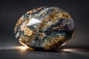 Raue Pietersite-Kristalle mit braunen und blauen Farbverl auf dunklem Hintergrund, symbolisiert Transformation und innere Kraft.