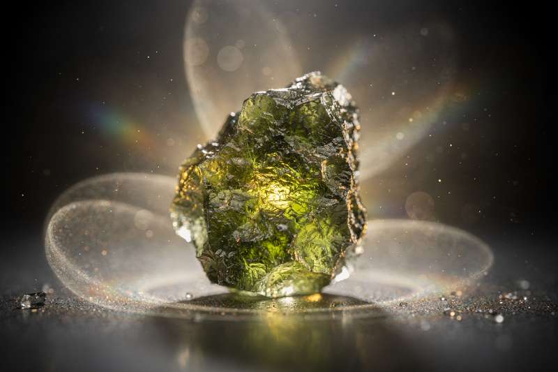 Grüner Moldavit-Kristall mit glatter Oberfläche auf neutralem Hintergrund, symbolisiert spirituelle Transformation und...
