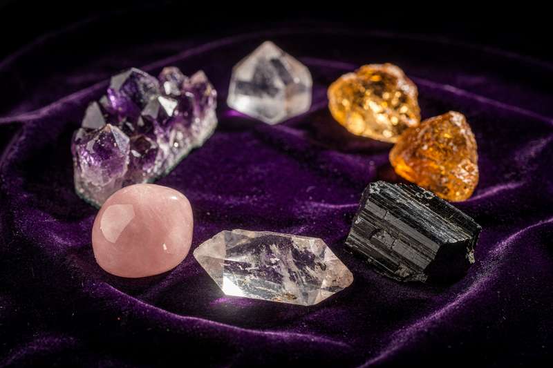 Verschiedene Heilkristalle und Mineralien in unterschiedlichen Farben und Formen liegen nebeneinander auf einer hellen Oberfläche.